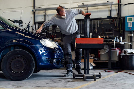 Auto technician checking headlight by car at repair garage