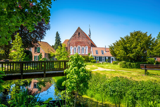 Germany, Lower Saxony, Krummhorn, Small bridge over standing water with Loquard church in background