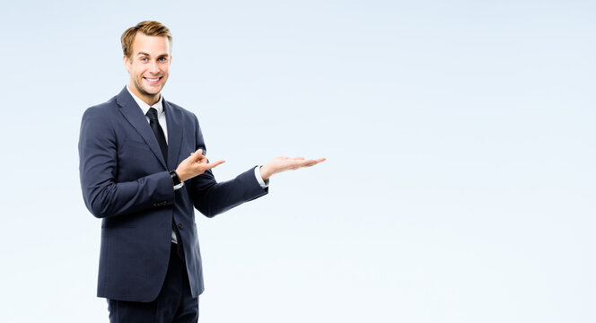 Businessman in suit showing, holding, giving some product or copy space area for advertising text, isolated on grey background. Young happy corporate business man at studio image. Professional person.