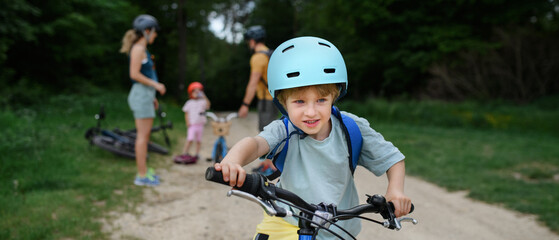Portrait of excited little boy with his family at backround riding bike on path in park in summer