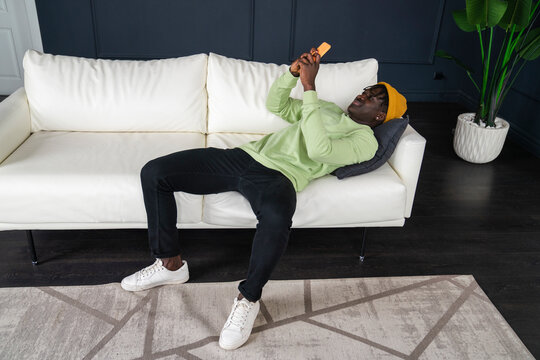 Young man using smart phone lying on sofa at home