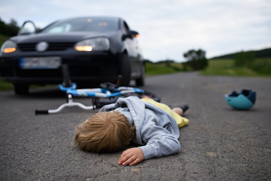 Little boy fallen from bicycle and lying still on road after car accident.
