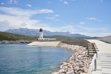 Path leading to the lighthouse against the backdrop of mountains and blue sky