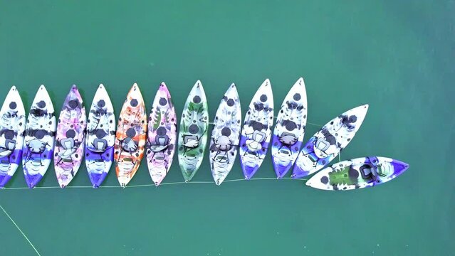 A dynamic top-down aerial shot of colorful kayaks or small watercrafts that are tied up neatly and ready to be rented by tourists. Sai Kung is known for its quaint fishing villages and fresh seafood.