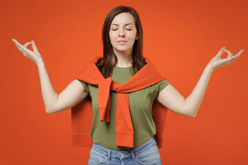 Young spiritual woman 20s wear khaki t-shirt tied sweater on shoulders hold spreading hands in yoga om aum gesture relax meditate try to calm down isolated on plain orange background studio portrait