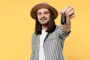 Young smiling happy fun man he 20s wears striped grey shirt white t-shirt hat hold in hand give car keys fob keyless system isolated on plain yellow color background studio. People lifestyle concept.