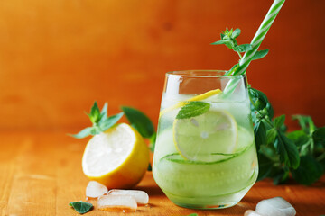 A glass of cucumber cold detox lemonade with mint and lemon on a wooden table