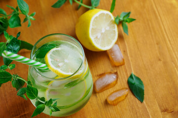 A glass of cucumber cold detox lemonade with mint and lemon on a wooden table
