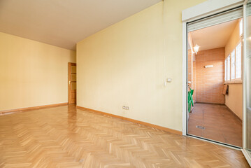 Empty living room in a house with herringbone oak parquet, woodwork and exit to a covered drying terrace and light yellow painted walls