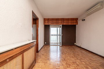 Empty living room with oak parquet floors, wooden radiator cover and white and brown painted walls