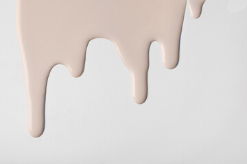Light brown liquid drops of paint color flow down on isolated white background. Abstract beige backdrop