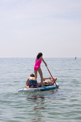 Three kids enyoying with a paddle surf in the sea on a summer day