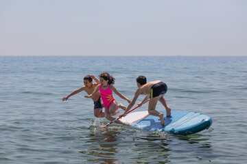 Three kids falling off a paddle surf on a summer day