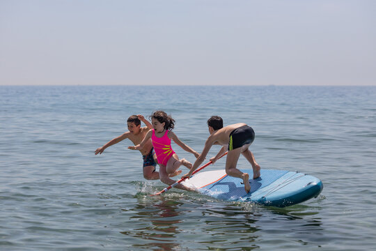 Three Kids Falling Off A Paddle Surf On A Summer Day