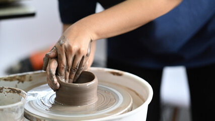 Fototapeta na wymiar Close up view woman creating handmade ceramic bowl on pottery wheel in workshop. Indoors lifestyle activity, handicraft, hobbies concept