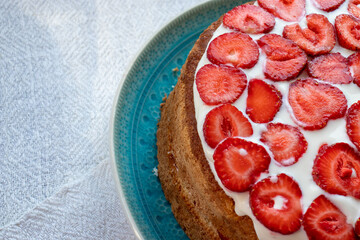 Cake with strawberries and cream on blue plate. Summer Strawberry and Cream sponge Layer Cake on white table cloth background. Top view, copy space. Midsummer food dessert