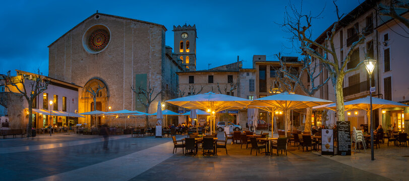 View of Santa Maria Church and people outside bar in Placa Mayor in the old town of Pollenca at dusk, Pollenca, Majorca, Balearic Islands
