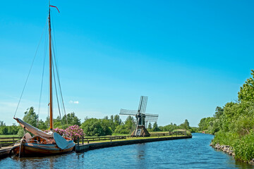 Typical dutch landscape, a traditional boat, an old windmill at a canal in Friesland in the Netherlands in spring