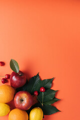 Summer vibes with green leaves and organic fruits on a orange background. Minimal flat lay.