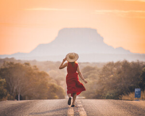 Mulher de chapéu e vestido caminhando na estrada com morro ao fundo no por ro sol- foto na ...