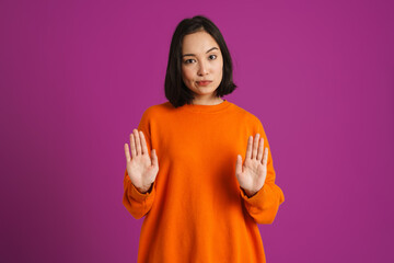 Young asian woman frowning while making winner gesture