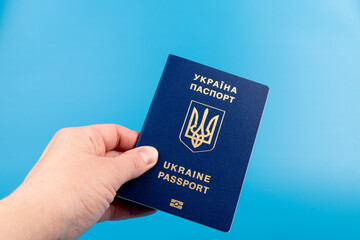 Passport of a citizen of Ukraine in a female hand on a blue background, close-up. Inscription in Ukrainian Ukraine Passport