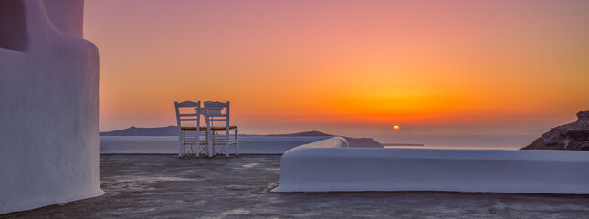 White architecture in romantic sunset light on Santorini island, Greece. Couple chairs on caldera...