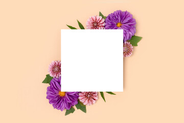 Square paper card mockup with border frame made of dahlia flowers on a beige background. Floral layout with copyspace.