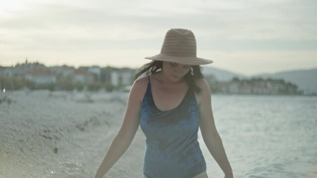 Caucasian girl in a hat and swimsuit walks on the beach by the sea. Beautiful woman close-up and slow motion video, happy and smiling man on vacation.