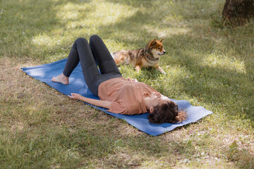 a European woman with meditates in the park with her dog on a blue yoga mat. shavasana and...