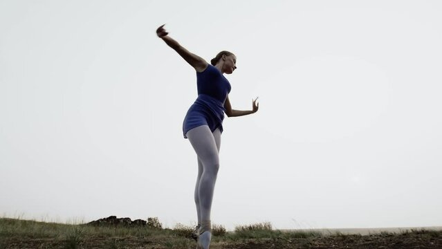 Professional dancer jumps up and starts spinning in pointe shoes, outdoor. Caucasian ballerina dances against the sky in sports dress. Concept of dance creativity and choreography