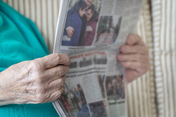 wrinkled hands of old person holding newspaper