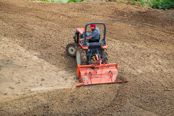 A farmer on a mini tractor loosens the soil for the lawn. Land cultivation, surface leveling