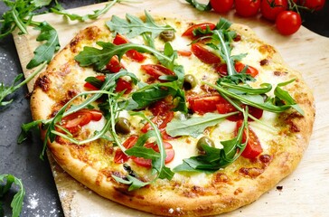 Freshly baked pizza with arugula, tomato, olive,  hollandaise sauce and mozzarella