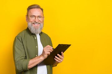 Portrait of cheerful friendly aged person hold clipboard pen empty space isolated on yellow color background
