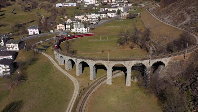 Train on Brusio Spiral Viaduct in Switzerland on Sunny Day. Bernina Railway. Swiss Alps. Aerial View. Drone Flies Forward, Tilt Down