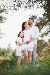 Obraz premium Happy pregnant couple with daughter in summer nature.