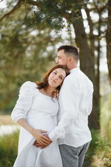 Happy and young pregnant couple hugging in nature