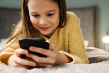 White happy girl using mobile phone while lying on bed