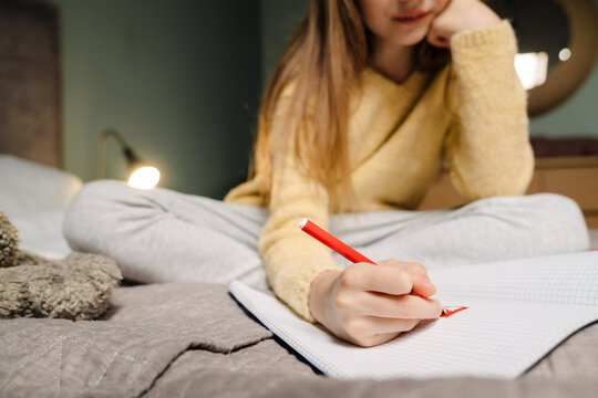 White blonde girl doing homework while sitting on bed