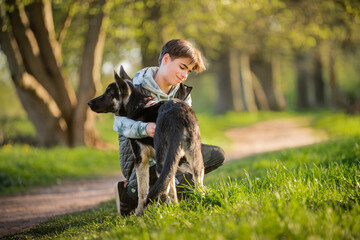 a boy with a dog walks in the park on a sunny spring evening, sits on the grass, the dog obeys the order give a paw. Friendship of man and animal, healthy lifestyle.