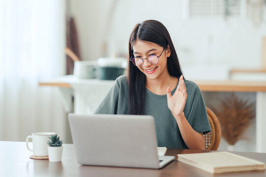 
Happy positive young asian woman enjoying online communication at home, Female using wifi while video conferencing with friend, sitting in front of open laptop, smiling and waving hand, saying hi