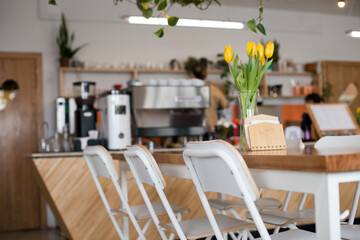Cafe interior close up with wooden table and stools or chairs with flowers - yellow tulips bouquet in the vase. Interior design of cafe or restaurant in modern minimal style, Scandinavian eclectic