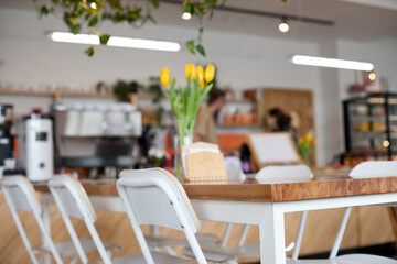 Cafe interior close up with wooden table and stools or chairs with flowers - yellow tulips bouquet...