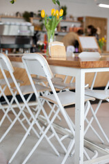 Cafe interior close up with wooden table and stools or chairs with flowers - yellow tulips bouquet in the vase. Interior design of cafe or restaurant in modern minimal style, Scandinavian eclectic