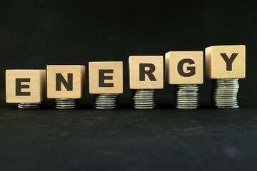 Energy crisis and high price of fuel, oil, gas and and petrol concept. Increasing stack of coins in wooden blocks with word energy on dark black background.
