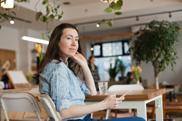 Young beautiful woman using mobile phone to browse social media sitting at cafe or coworkring space, smiling. Candid lifestyle photo of female using technology