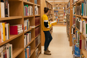 Young female student reading a book from wooden bookshelves in university library. Woman in public...