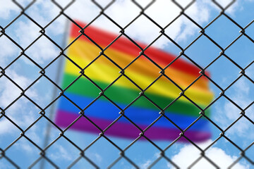 A steel mesh against the background of a blue sky and a flagpole with flag of lgbt pride