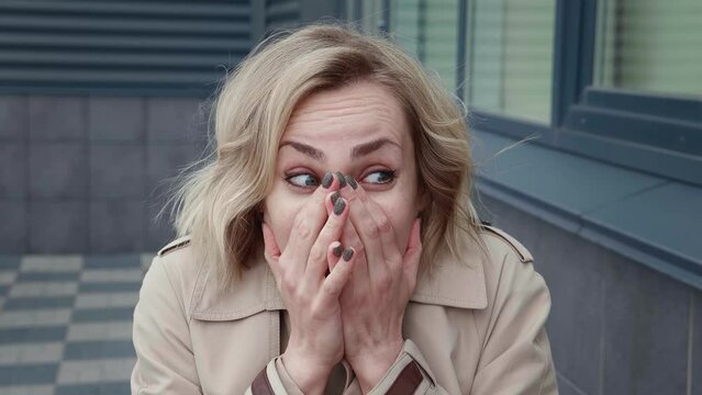 Portrait of shocked woman from fright covers her mouth with her hands, standing near an office building. Surprised caucasian female with terrible news, standing outdoors